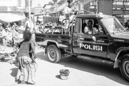 Eine Straßenszene. Eine Frau, die wir von hinten sehen, steht barfuß, wie aus voller Bewegung angehalten vor einem schwarzen Pick-Up-Truck, auf dessen Tür 